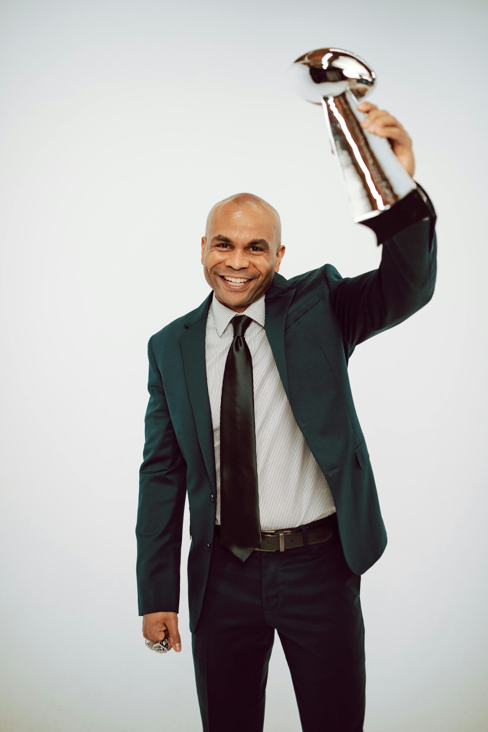 Happy man in a suit holding a trophy, celebrating achievement, isolated on a white background.